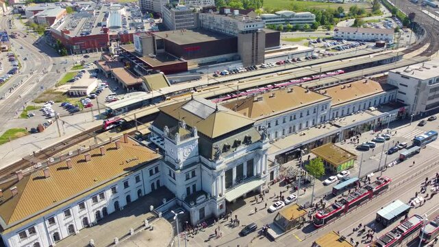 Aerial view from above, Brno's Central Train Station on a sunny day, with lots of people and traffic on roads.