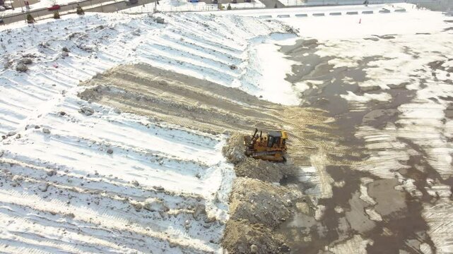 Drone flies from right to left, backhoes machine clearing snow near highway during day. Montr&eacute;al, Qu&eacute;bec, Canada.