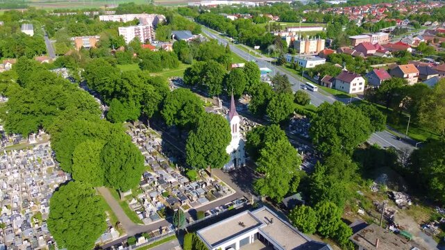 A drone zooms in to cityscape of Kapuvar, Hungary, featuring streets, tower, buildings, houses, highway, and green trees.