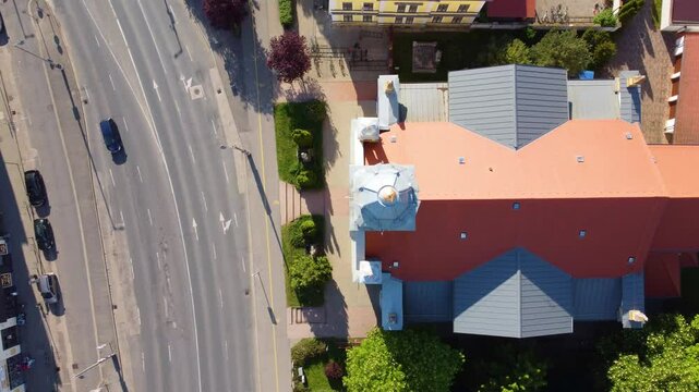 Drone flies over church, its roof, highway, and houses and trees behind it in Slovenska Bistrica, Slovenia.
