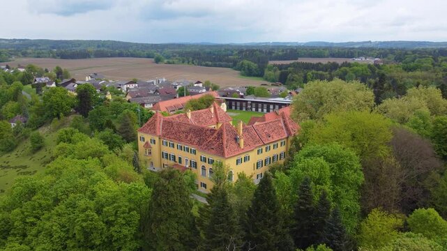 Leibnitz, Austria. Drone flies in from above, Launegg Castle surrounded by green trees and sky. Closeup shows yellow castle's windows and gateway.