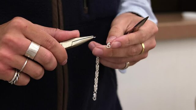 Jeweller standing in shop using pliers to make silver bracelet for selling.