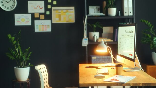 Desk with computer, lamp, documents and coffee cup in modern office with no people. Zoom-off shot