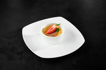 Crème Brûlee with Fresh Strawberry on White Plate Against Dark Background