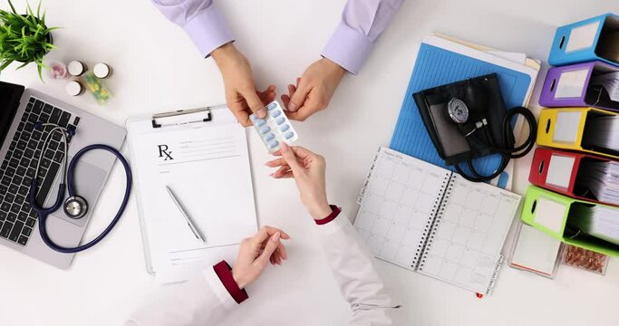 Female doctor gives capsules to male patient sitting at desk
