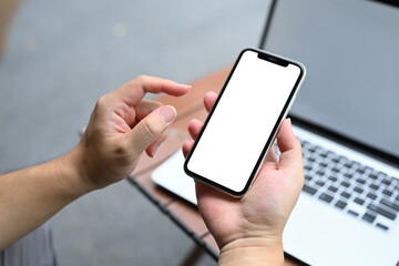 Man holding mobile phone sitting in front of laptop at outdoor cafe. Empty screen for your advertising text