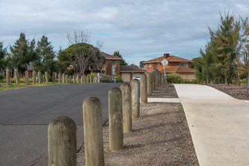Wooden bollards divide the road from the footpath,  segregating traffic and pedestrians. Timber barrier posts along the walkway in a suburban neighborhood with houses.