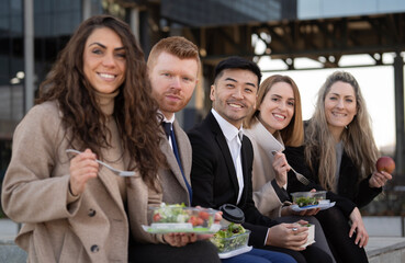 Side view of diverse business people enjoying a lunch break outdoor from office building and looking at camera