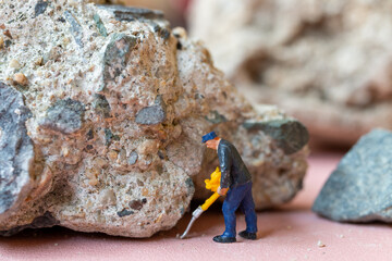 A miniature worker worker drilling a big rock . Themes of perseverance, strength and labor. This makes it suitable for use in content that involves hard work, challenges, and overcoming obstacles.
