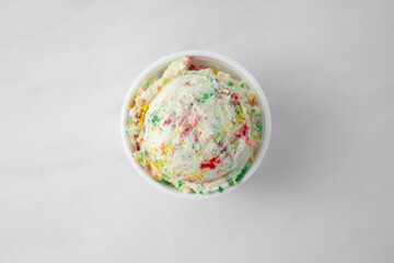 A top down view of one small scoop of birthday cake ice cream in a styrofoam cup.