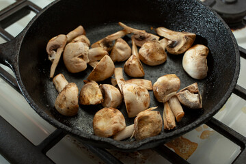 A view of a quartered button mushrooms sauteing in a cast iron skillet.