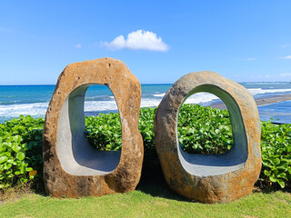Two large, rough-hewn stone sculptures with oval cutouts stand on a lush green lawn, overlooking a...