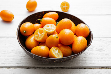 Kumquats or cumquats ( Citrus japonica) inside a coconut bowl and on white wood board background. Studio shot, studio light.