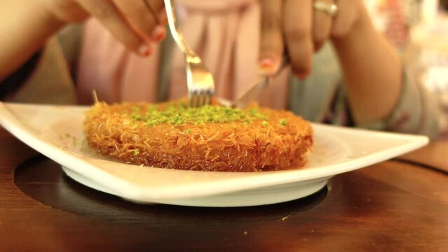 woman eating Turkish dessert kunefe, kunafa, kadayif with pistachio 