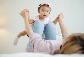 Naklejka premium Young daughter plays with asian cute mother lying on the bed that mother held her daughter's hand and spread it out and imagined herself to be like an airplane enjoy flying in the air.