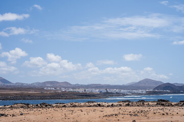 Views of the village of La Santa from the coast. Seascape. White sand beach and rocks. Mountains in the background. Sea coast.  Sky with big white clouds. Lanzarote, Canary Islands, Spain