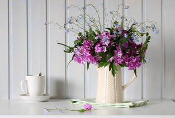 a bouquet of primroses and forget-me-nots in a jug on the table in a white wooden cottage. springtime, rural composition.