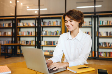 Young smiling cheerful happy successful employee IT business woman wear white shirt casual clothes hold use work on laptop pc computer surfing internet sit at office desk. Achievement career concept.