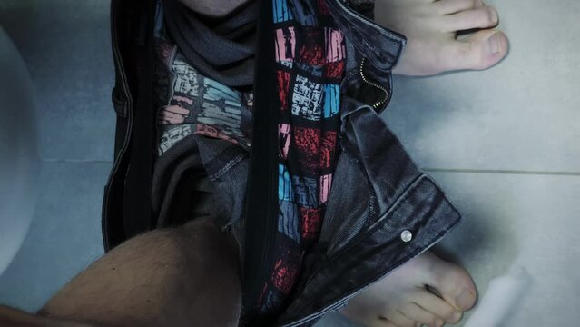 Man with bare feet sitting on toilet and drops toilet paper. Vertical video