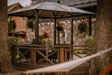 Blome, Latvia - September 11, 2023 - Charming outdoor gazebo with hanging plants and decorative lights, surrounded by trees, creating a cozy and inviting garden space. Copy space...
