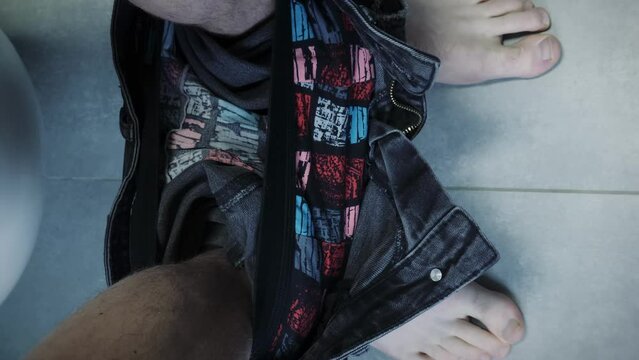 Male in jeans and underwear with bare feet sits on white toilet. Vertical video