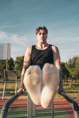 Calisthenic man doing L-sits on street workout bars. Focused young man with tattoos exercising on...