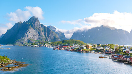 A panoramic view of a charming village nestled amidst towering mountains and a sparkling fjord in...