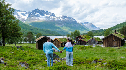 A couple walks hand in hand in front of traditional Norwegian cabins with a stunning mountain backdrop. Innerdalen Norway most beautiful mountain valley