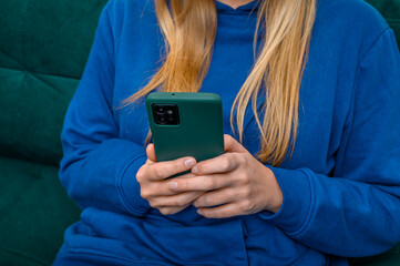 Zbuntowana nastolatka siedzi na kanapie i wpatruje się w swój smartfon