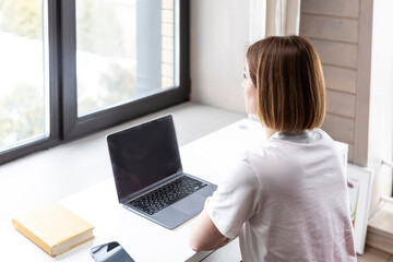 Fototapeta premium Back view on Young female student sitting at the desk at home and preparing for a new academic year. Education and online training concept