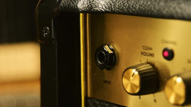 Close-up of plugging a jack into a guitar amplifier and turning up the volume knob