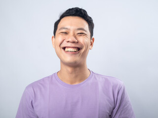 Young Asian man in a lavender t-shirt smiling warmly at the camera. Studio shot on a plain...