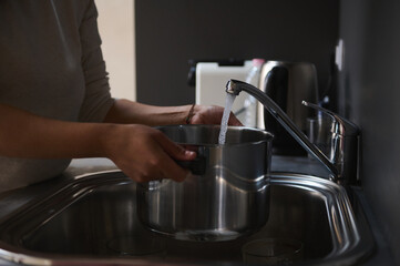 Person filling pot at kitchen sink with running water