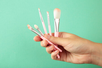 Female hand with make-up artist brushes on mint background