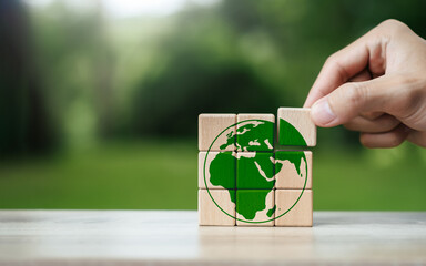 Environment World Earth Day Concept. Hand placed wooden block of green globe icon. Green business...