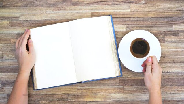 Hands open book on empty page, top view of the desk wuth coffee