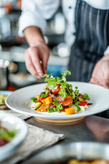 Chef adding final touches to a colorful gourmet dish with microgreens in a professional kitchen..