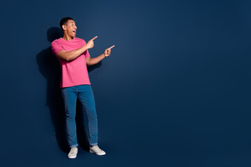 Photo of young funky positive man in pink t shirt pointing fingers billboard price falling isolated on dark blue color background