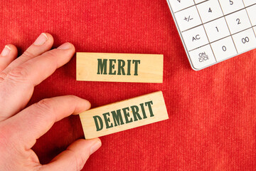 Business and demerit or merit concept. Copy space. Concept word Demerit or Merit on the blocks assembled by hand in a composition with a calculator on a red background, top view