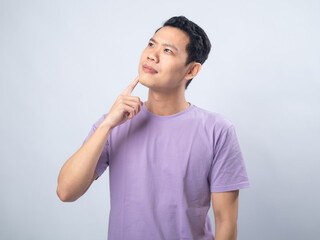 Young Asian man in a lavender t-shirt looking thoughtful with his finger on his chin. Studio shot...