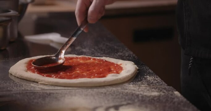 Pizza chef smears the pizza dough with tomato paste