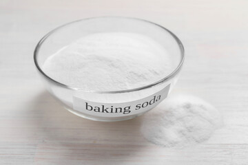 Baking soda in bowl on white wooden table, closeup