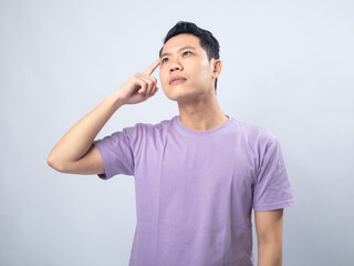 Young Asian man in a lavender t-shirt looking thoughtful with his finger on his chin. Studio shot on a plain background, highlighting his contemplative expression and casual fashion.