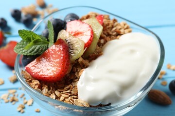 Tasty granola with berries, yogurt and mint on light blue wooden table, closeup
