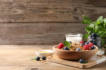 Tasty granola with berries, nuts and mint on wooden table, space for text