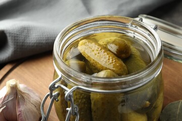 Pickled cucumbers in jar on wooden board, closeup