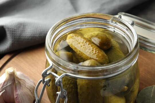 Pickled cucumbers in jar on wooden board, closeup
