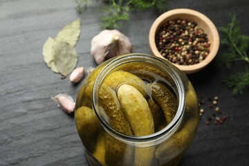 Pickled cucumbers in open jar and spices on dark textured table, closeup