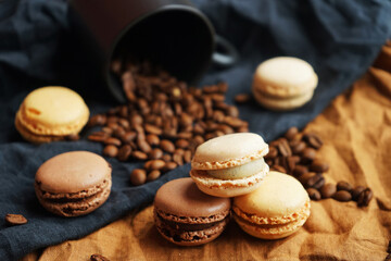 Coffee beans next to a black cup and macarons on linen black and brown towels on a dark background