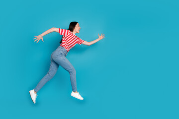 Full length photo of charming positive girl wear striped t-shirt jumping high running empty space isolated blue color background